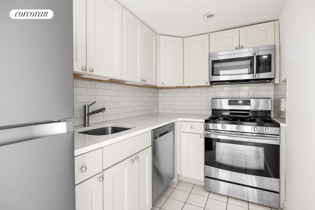 201 E 28th St Unit 16G, New York City, NY 10016 - kitchen featuring stainless steel appliances, a sink, light countertops, white cabinets, and tasteful backsplash