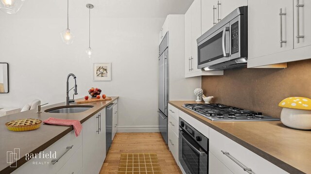 kitchen featuring pendant lighting, sink, stainless steel appliances, white cabinets, and light wood-type flooring