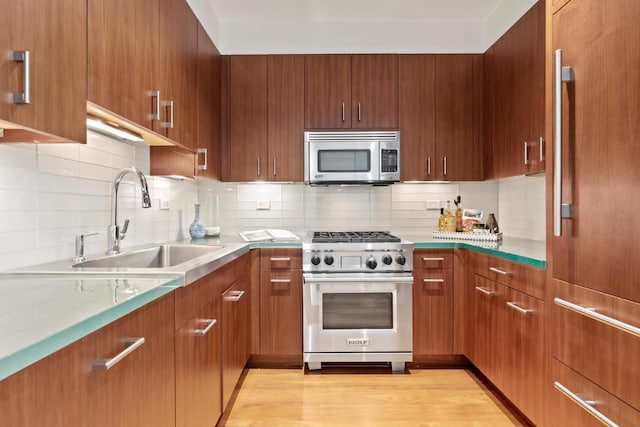 kitchen featuring premium appliances, light wood-type flooring, decorative backsplash, and a sink