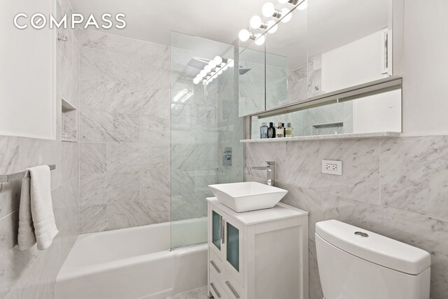 full bathroom featuring toilet, tiled shower / bath, tile walls, vanity, and a notable chandelier