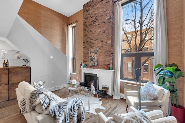 living area featuring a lit fireplace, wood finished floors, and a towering ceiling