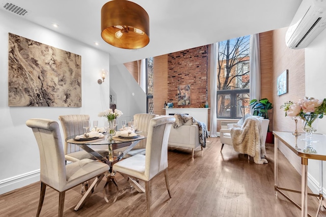 dining space with visible vents, a wall mounted AC, baseboards, and wood finished floors