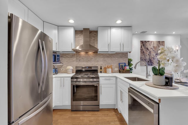 kitchen with a sink, stainless steel appliances, light countertops, white cabinets, and wall chimney exhaust hood