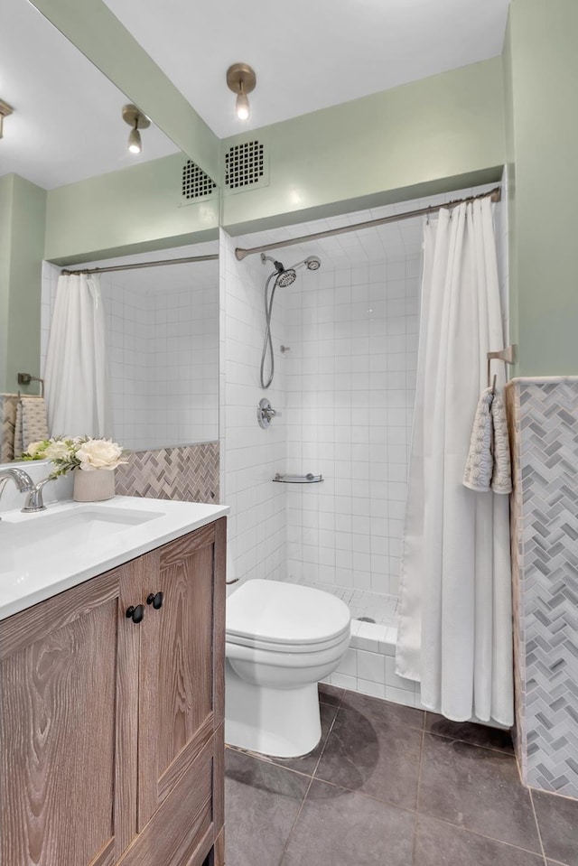 full bath with vanity, tiled shower, tile walls, toilet, and tile patterned floors