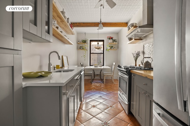 kitchen featuring open shelves, gray cabinets, appliances with stainless steel finishes, a sink, and wall chimney range hood