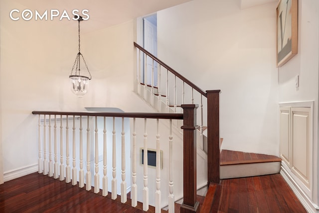 stairs with baseboards, hardwood / wood-style floors, and an inviting chandelier