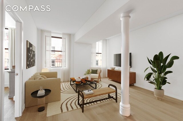 living area featuring baseboards, ornate columns, and wood finished floors