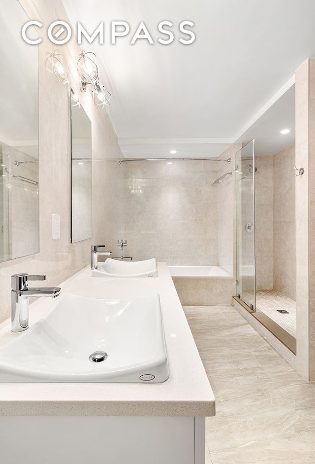 full bath with double vanity, tile walls, a shower stall, and a sink