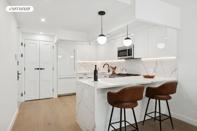 428 E 9th St Unit 201, New York City, NY 11218 - kitchen with stainless steel microwave, a peninsula, white cabinetry, a breakfast bar area, and light wood finished floors