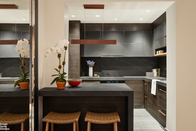 kitchen featuring modern cabinets, a kitchen bar, dark countertops, tasteful backsplash, and recessed lighting