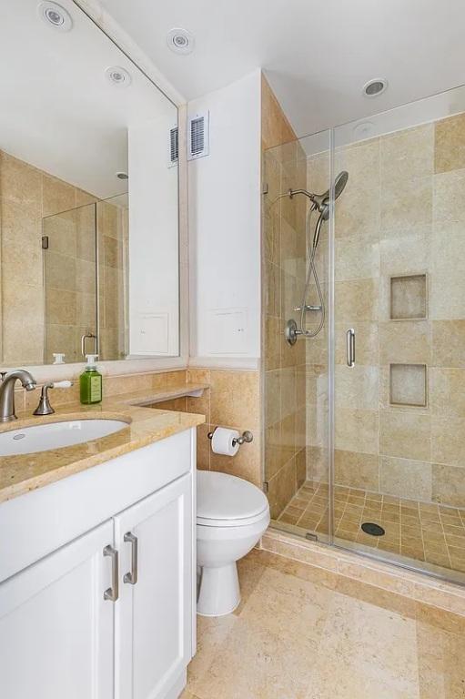 bathroom with tile walls, visible vents, toilet, a shower stall, and vanity