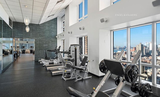 gym featuring a towering ceiling, baseboards, a drop ceiling, and a city view