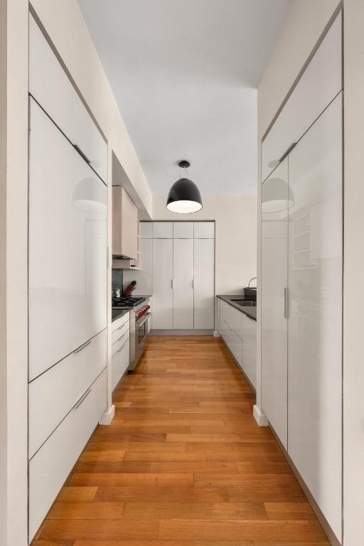 kitchen featuring high end stainless steel range oven, sink, light hardwood / wood-style floors, and white cabinets