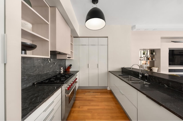 kitchen with open shelves, stainless steel range, a sink, light wood finished floors, and backsplash