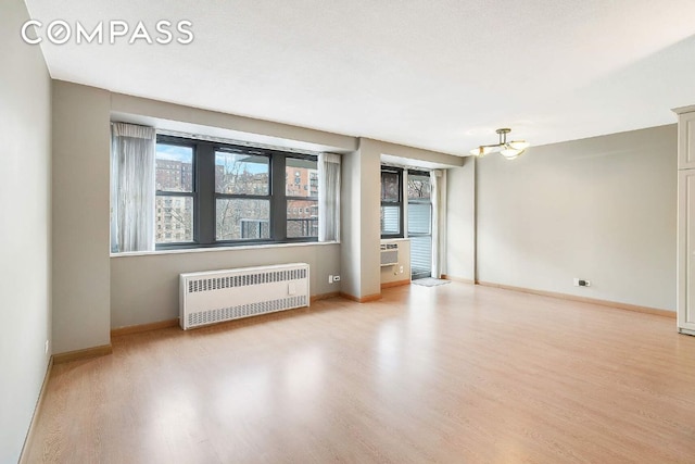 spare room with an inviting chandelier, radiator heating unit, and light hardwood / wood-style floors