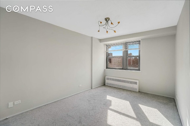 carpeted empty room with radiator and a notable chandelier