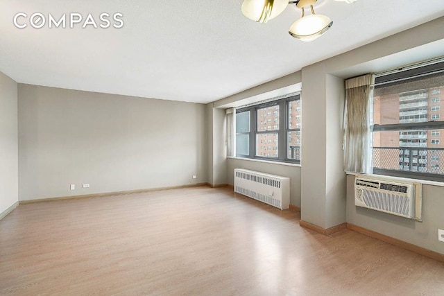 spare room featuring baseboards, radiator heating unit, and light wood-style floors