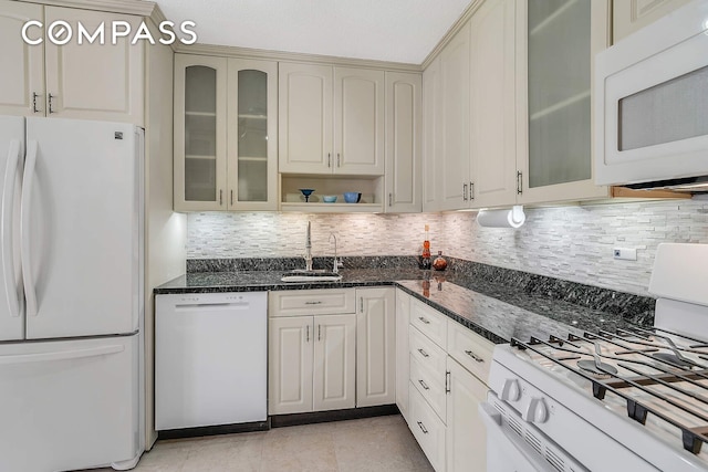 kitchen featuring dark stone counters, white appliances, a sink, and backsplash