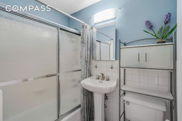 full bathroom with sink, combined bath / shower with glass door, tile walls, backsplash, and toilet