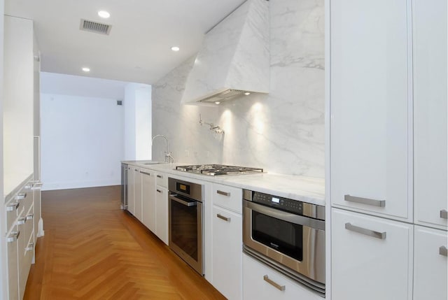 kitchen featuring sink, white cabinetry, stainless steel appliances, custom exhaust hood, and light parquet flooring