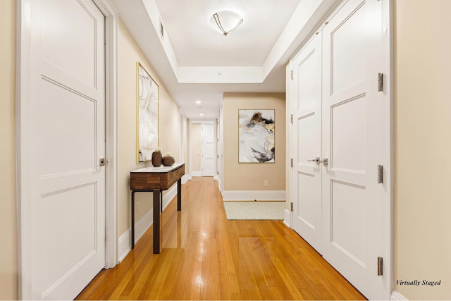 hallway with a raised ceiling, baseboards, and light wood finished floors