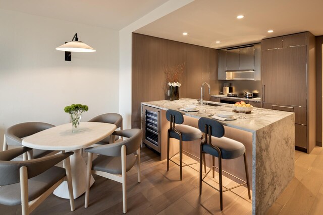 kitchen with sink, beverage cooler, light stone counters, and light wood-type flooring