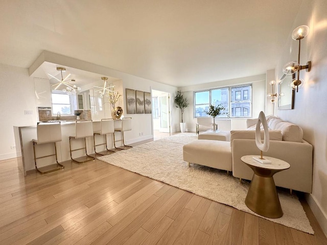 living area featuring light wood finished floors, baseboards, and a notable chandelier