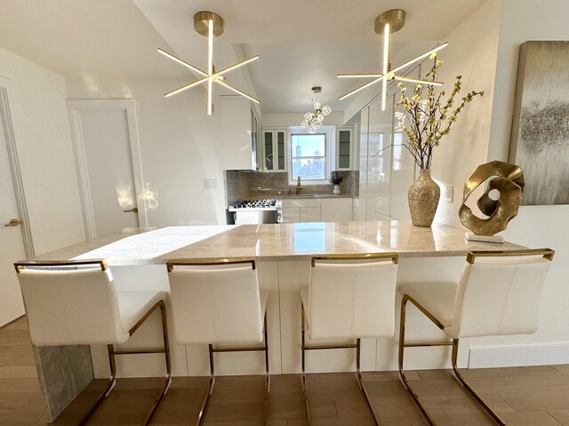 kitchen with tasteful backsplash, white cabinets, hanging light fixtures, light stone counters, and an inviting chandelier