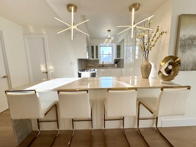 kitchen featuring decorative backsplash, glass insert cabinets, a kitchen breakfast bar, an inviting chandelier, and white cabinetry