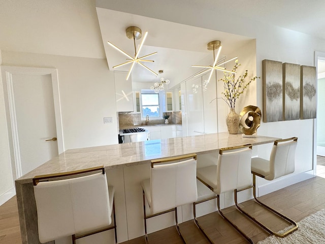 kitchen with white cabinets, a sink, a breakfast bar area, wood finished floors, and backsplash