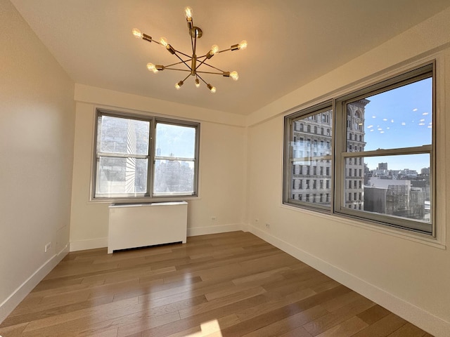 spare room with radiator, an inviting chandelier, baseboards, and wood finished floors