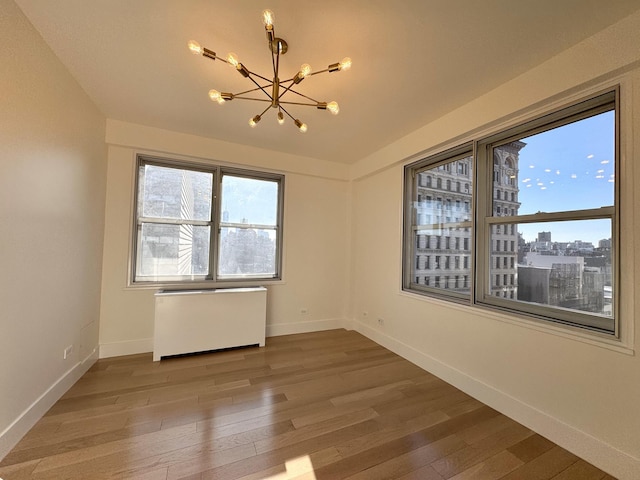 empty room featuring wood-type flooring, baseboards, a chandelier, and radiator heating unit