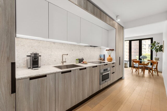 kitchen with backsplash, modern cabinets, a sink, and oven