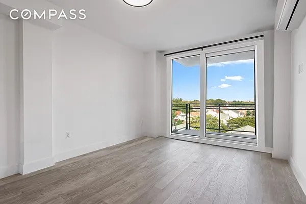 empty room featuring expansive windows, baseboards, an AC wall unit, and wood finished floors