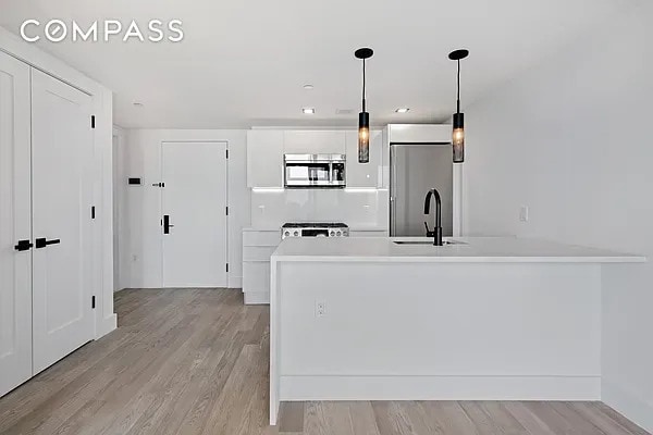 kitchen with a sink, a peninsula, light wood-style floors, and stainless steel appliances