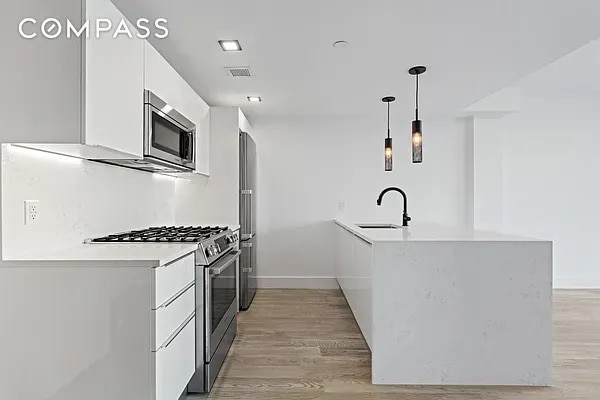 kitchen featuring a sink, white cabinetry, appliances with stainless steel finishes, a peninsula, and light wood finished floors