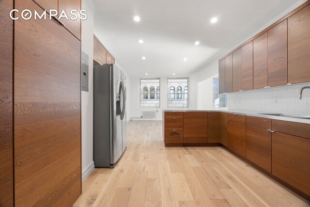 kitchen with stainless steel fridge with ice dispenser, decorative backsplash, light hardwood / wood-style floors, and sink