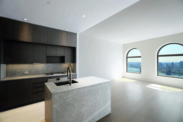 kitchen with stainless steel gas stovetop, an island with sink, sink, backsplash, and light hardwood / wood-style floors