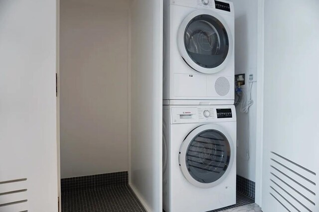 laundry area with light tile patterned floors and stacked washing maching and dryer