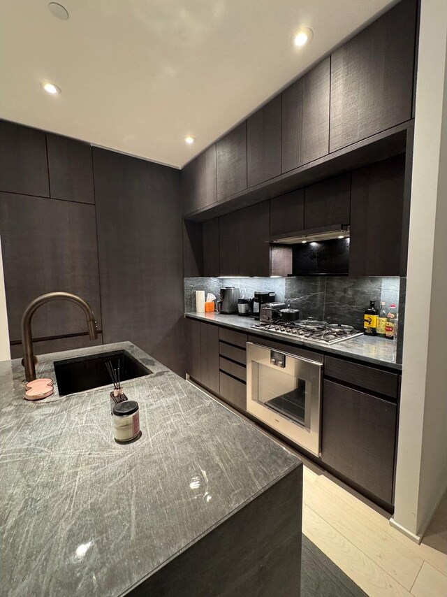 kitchen with sink, tasteful backsplash, oven, stainless steel gas stovetop, and light wood-type flooring