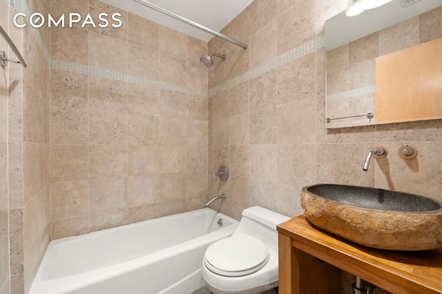 bathroom with a sink, tub / shower combination, toilet, and tile walls