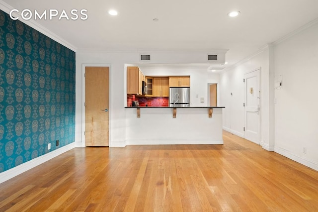 unfurnished living room featuring ornamental molding, light wood-type flooring, visible vents, and baseboards