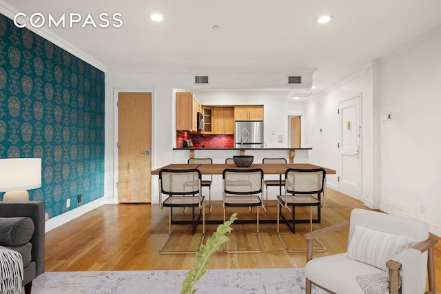 dining area featuring visible vents, crown molding, an accent wall, and wallpapered walls