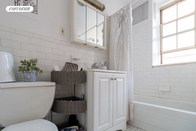 bathroom with a healthy amount of sunlight, toilet, shower / tub combo, and tile walls