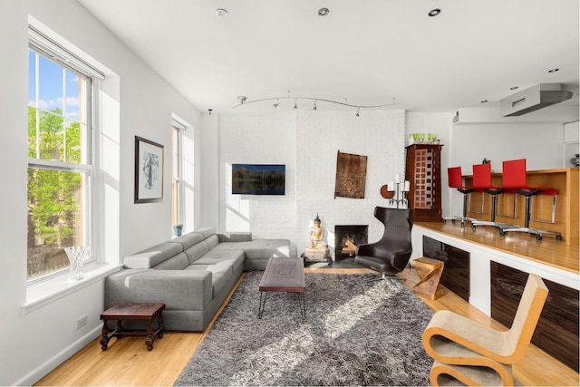 living room featuring rail lighting, a brick fireplace, and light hardwood / wood-style floors