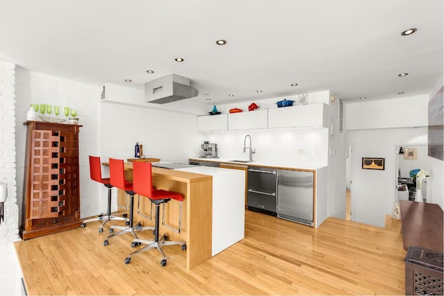 kitchen featuring white cabinetry, light hardwood / wood-style flooring, a kitchen breakfast bar, and refrigerator