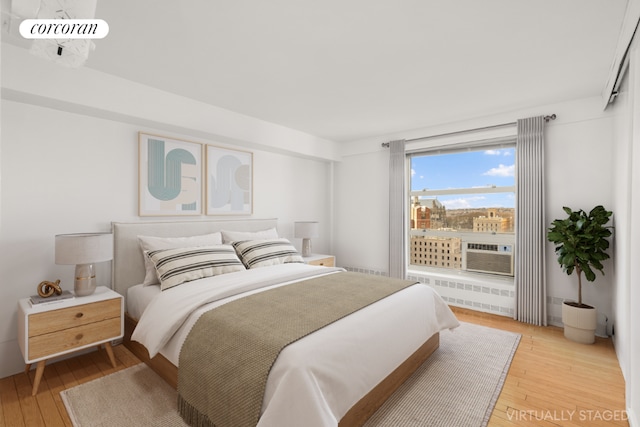 bedroom with cooling unit, radiator heating unit, and light hardwood / wood-style floors