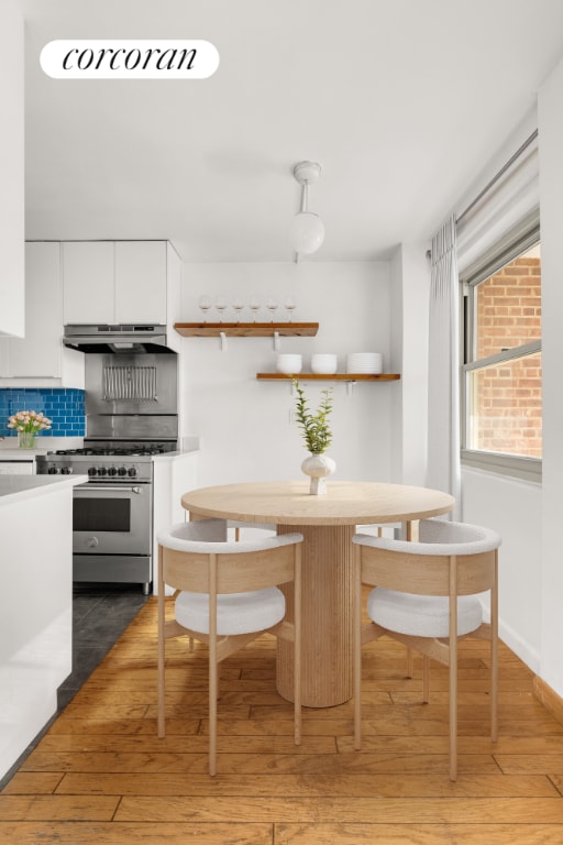 kitchen with tasteful backsplash, white cabinetry, high end stainless steel range, breakfast area, and dark wood-type flooring