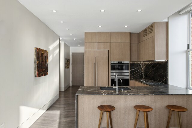 kitchen with appliances with stainless steel finishes, a breakfast bar, dark stone countertops, and kitchen peninsula