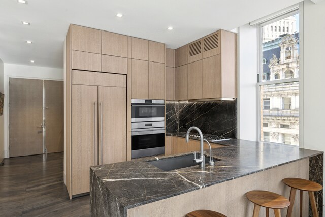 kitchen featuring sink, a breakfast bar area, dark stone counters, kitchen peninsula, and paneled refrigerator